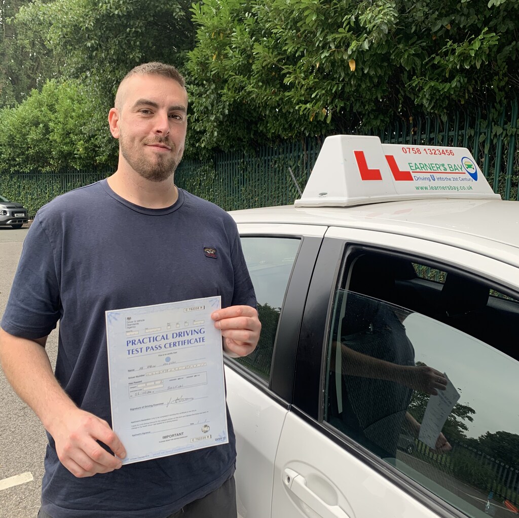 Learner holding a practical driving test pass certificate beside a car.