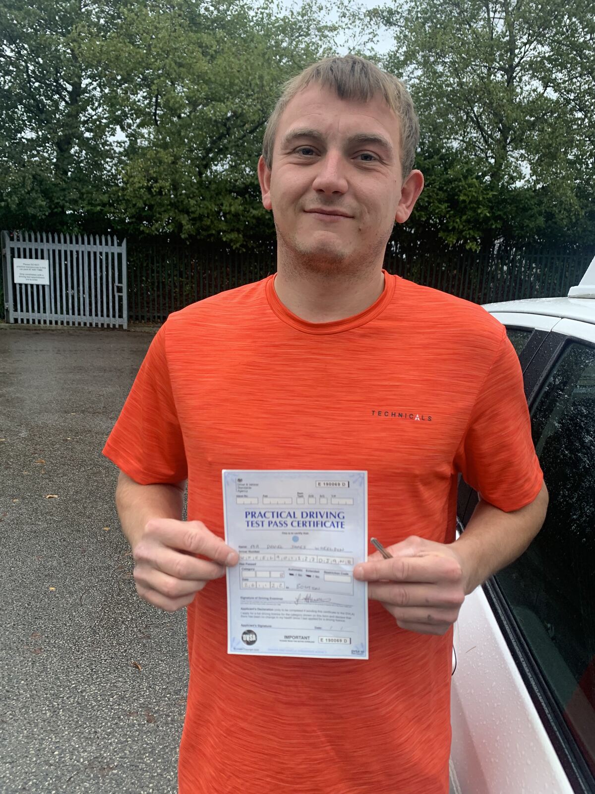 Learner holding a practical driving test pass certificate outdoors.